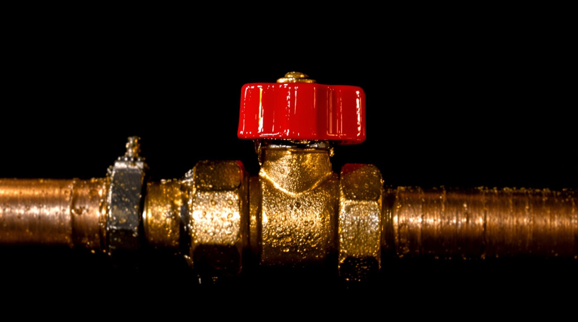 Brass ball valve with a red handle on a copper pipe, water droplets on the metal
